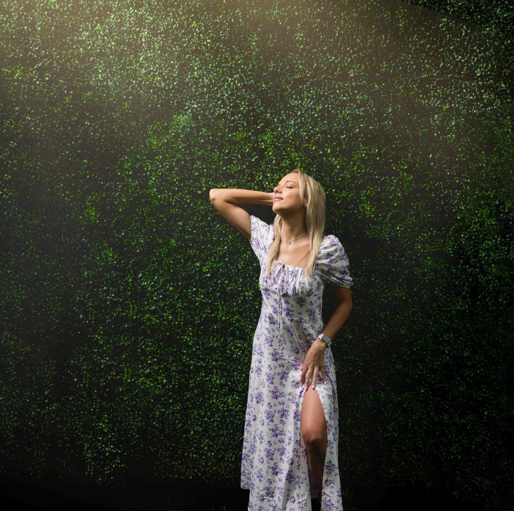 Case Studios Photography Senior girl posing in ray of sunlight against a greenery wall.