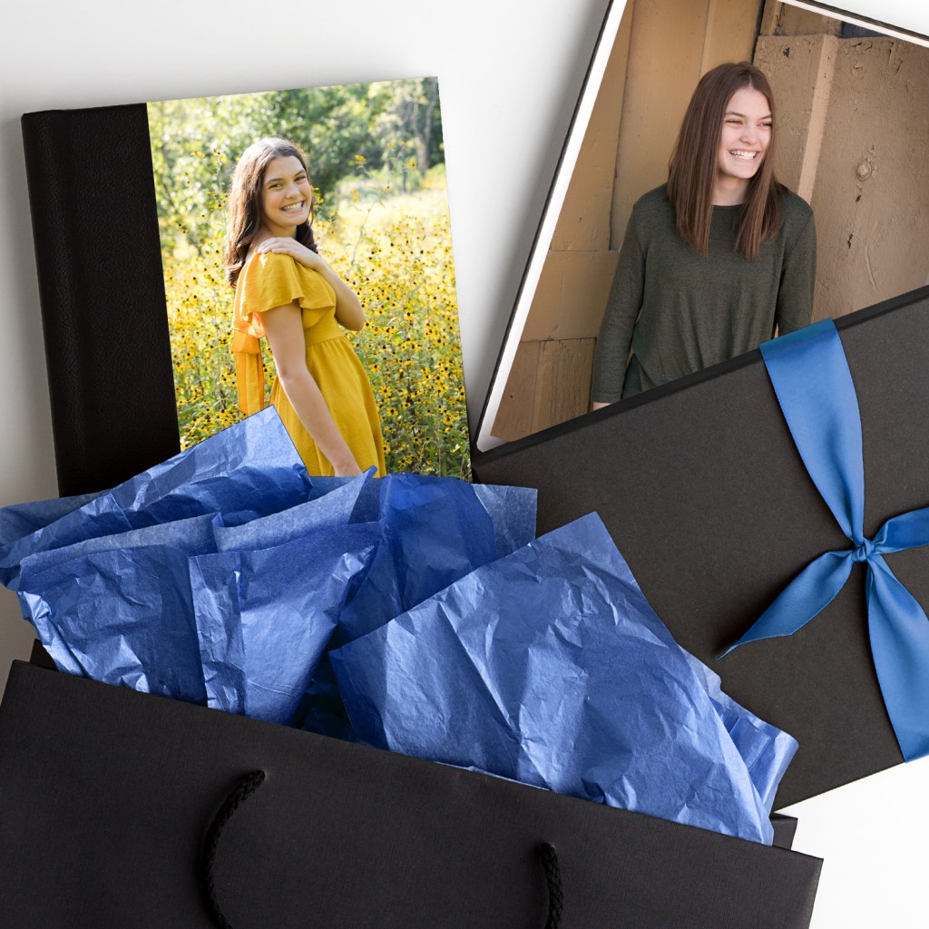 Gift with blue ribbon, photo album showing a woman in a yellow dress in a field, other photo of a smiling woman. Blue tissue paper inside.